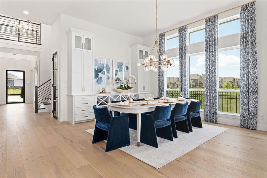 Dining area featuring light wood-style flooring, a towering ceiling, a chandelier, and stairway Dining area featuring light wood-style flooring, a towering ceiling, a chandelier, and stairway
