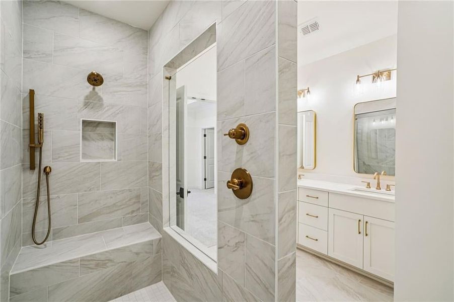 Primary spa bathroom features a large walk in shower, with drying area. Double vanity with upgraded cabinets, quartz and framed mirrors. Image is from previous unit