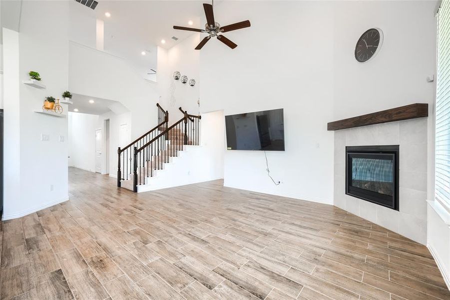 Unfurnished living room with a towering ceiling, a fireplace, wood tiled floors, ceiling fan, and stairway Unfurnished living room with a towering ceiling, a fireplace, wood tiled floors, ceiling fan, and stairway