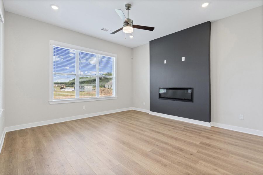 Spacious interior featuring wood-finish flooring and a contemporary linear electric fireplace inset into a dark accent wall Spacious interior featuring wood-finish flooring and a contemporary linear electric fireplace inset into a dark accent wall