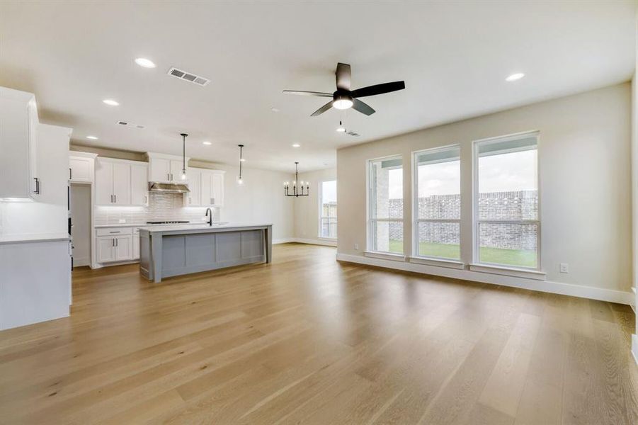 Open-concept living space featuring wood-finish flooring, a contemporary kitchen island with a sink, white cabinetry with modern hardware, and recessed ceiling lighting