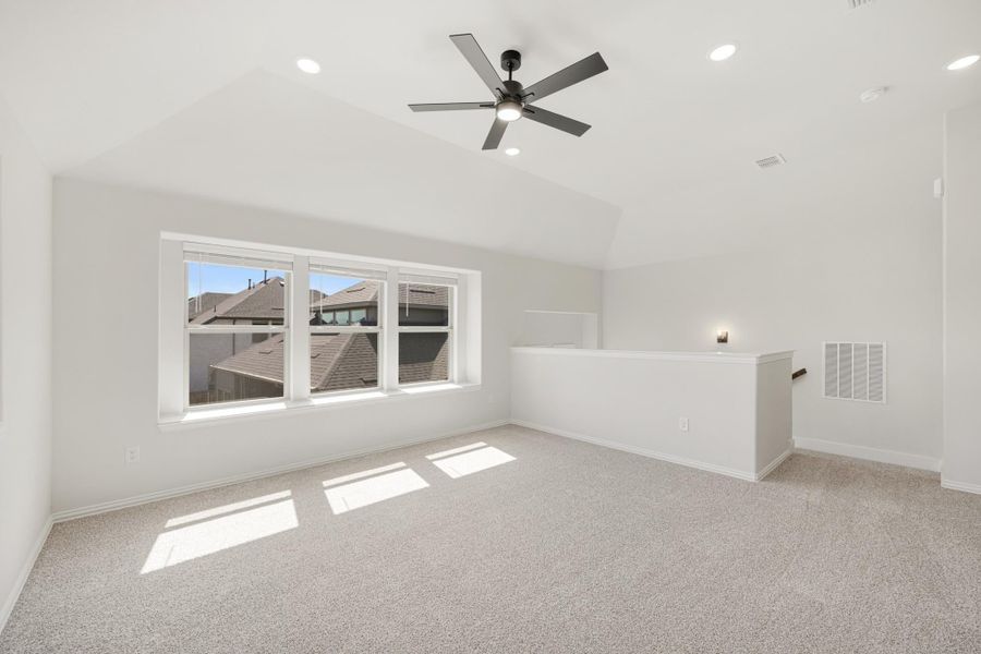 Open bonus room with vaulted ceiling, ceiling fan, carpet flooring, and triple windows overlooking neighboring rooftops
