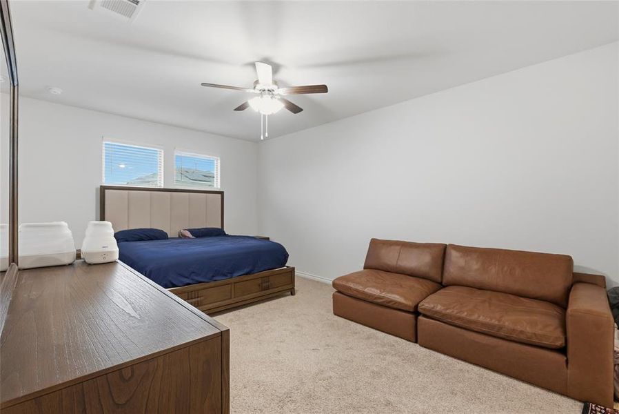 Spacious room featuring neutral carpeting, a ceiling fan with light fixture, and two transom windows with horizontal blinds