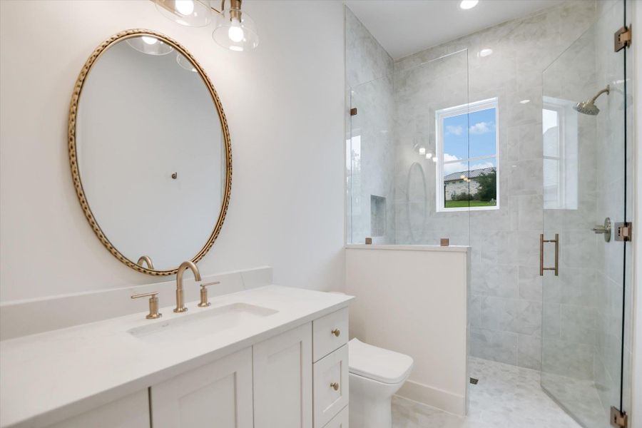Contemporary bathroom featuring a spacious glass-enclosed shower with tile surround and integrated window, white vanity with integrated sink and brushed gold fixtures, and an oval framed mirror