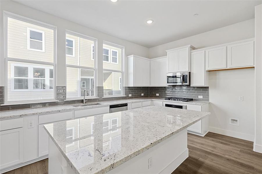 The kitchen features white cabinetry, a large central island with a light-colored countertop, and stainless steel appliances including a microwave and a range