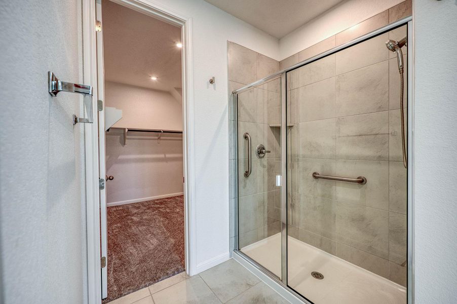 Tiled walk-in shower steps away from a carpeted walk-in closet.