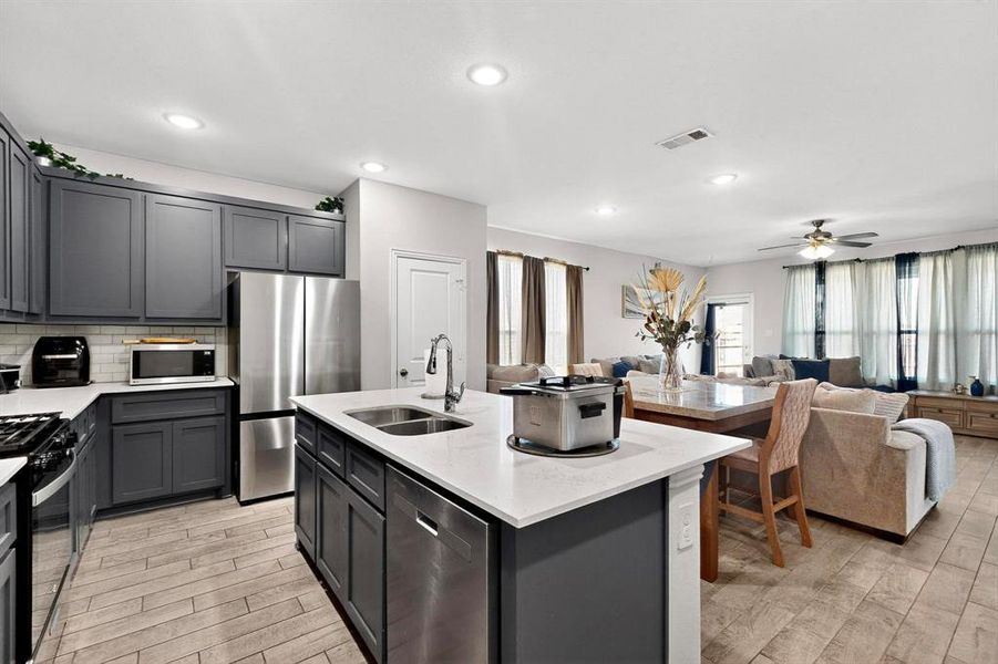 Kitchen featuring open floor plan, stainless steel appliances, light wood-type flooring, backsplash, and light stone counters Kitchen featuring open floor plan, stainless steel appliances, light wood-type flooring, backsplash, and light stone counters