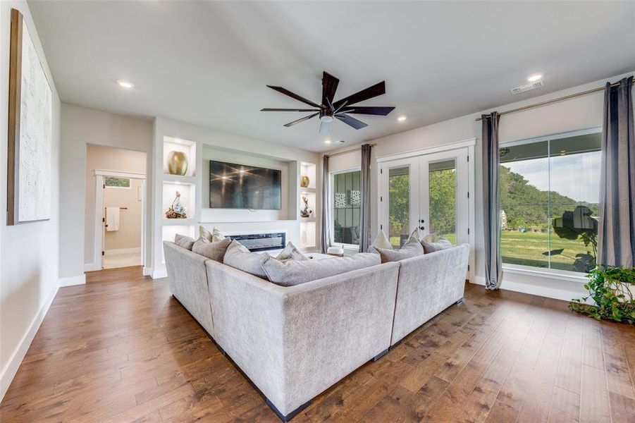 Living room with a glass covered fireplace, dark wood finished floors, ceiling fan, recessed lighting, and french doors