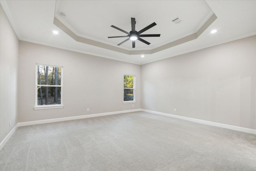 Primary bedroom with carpet and inset ceiling with lighted ceiling fan and crown molding.  Two double pane vinyl low E66 coating windows look to the back of the home.