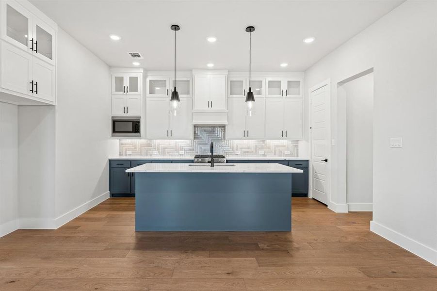 Kitchen with built in microwave, hanging light fixtures, tasteful backsplash, a kitchen island with sink, and white cabinets