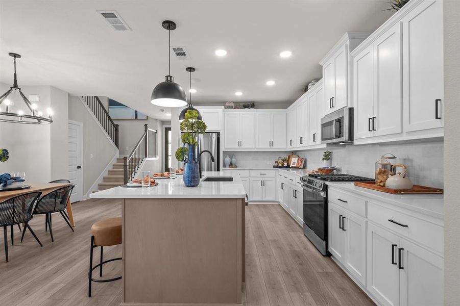 Two tone kitchen with stainless steel appliances, a kitchen island with sink, decorative backsplash, a breakfast bar, and light stone countertops
