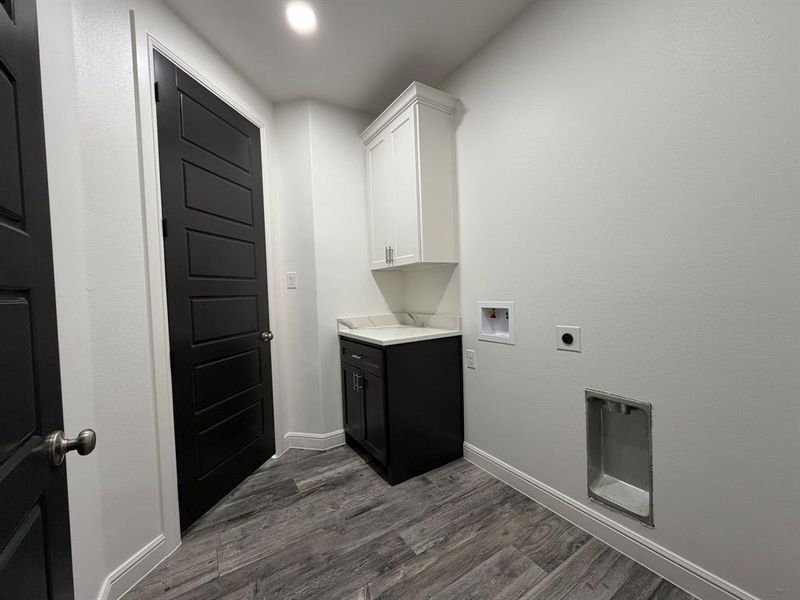 Laundry area featuring wood-finish flooring, white walls, and a corner vanity with a white countertop and dark cabinetry