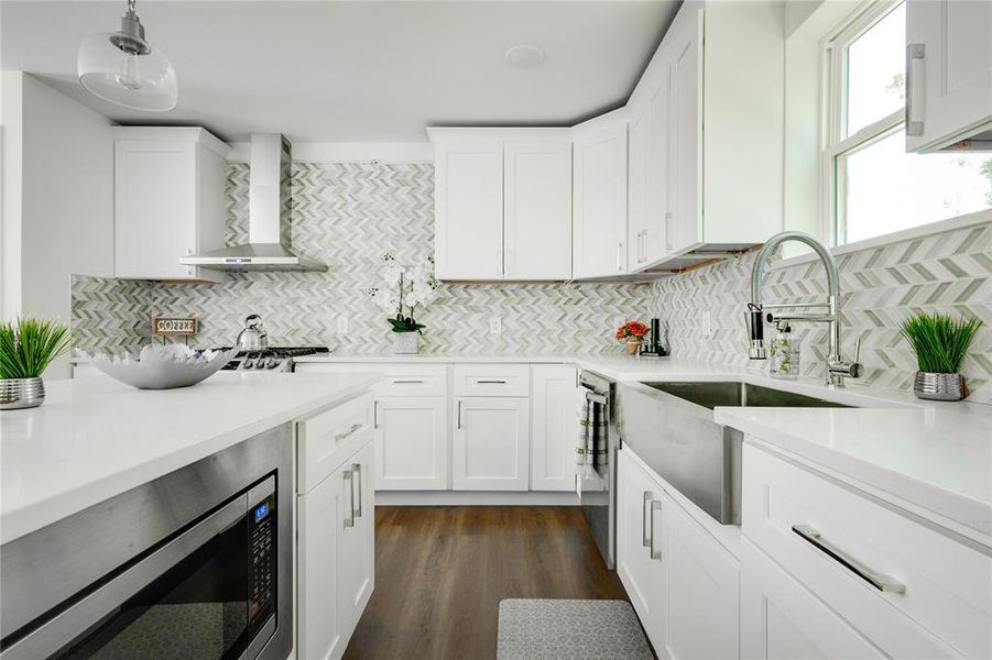 Kitchen with wall chimney exhaust hood, backsplash, stainless steel microwave, and dark wood-type flooring