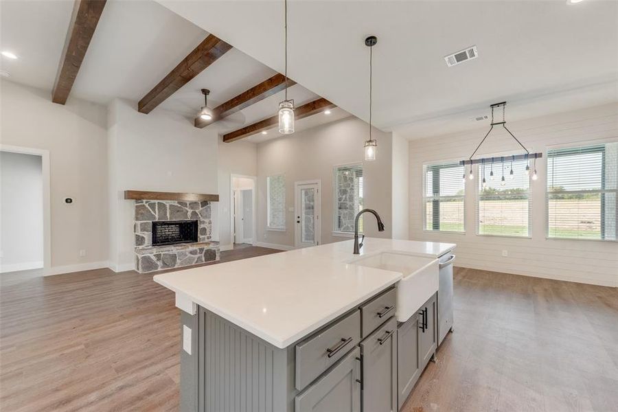 Kitchen featuring a kitchen island with sink, ceiling fan, pendant lighting, gray cabinets, and a stone fireplace