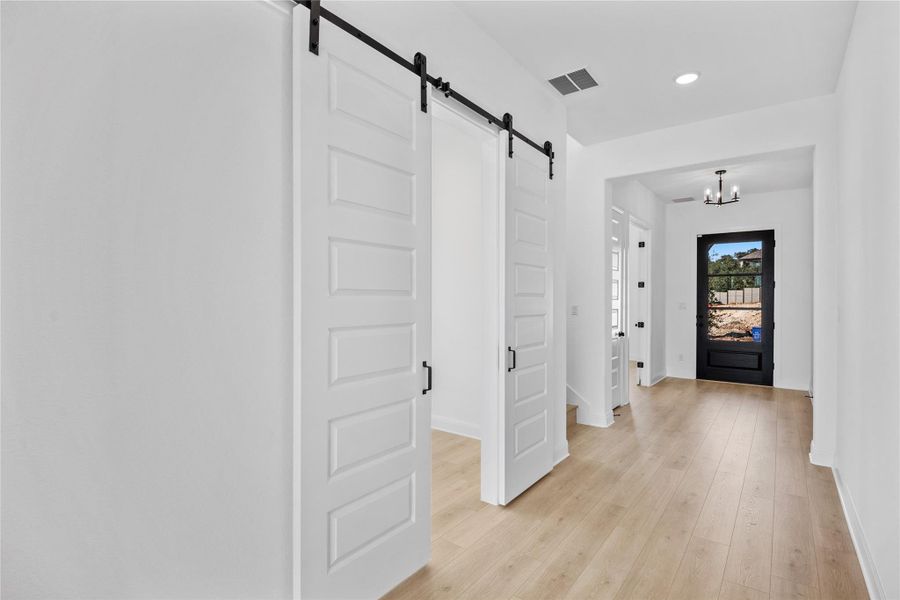 Hall with a barn door, light wood finished floors, and hanging lights