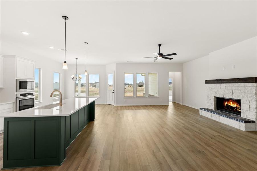 Kitchen with a fireplace, open floor plan, light wood finished floors, an island with sink, and dual tone cabinetry
