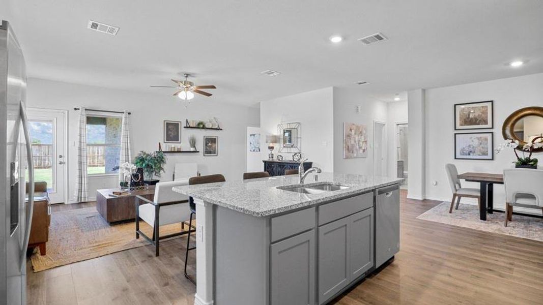 Kitchen featuring gray cabinetry, light stone countertops, ceiling fan, a center island with sink, and open floor plan