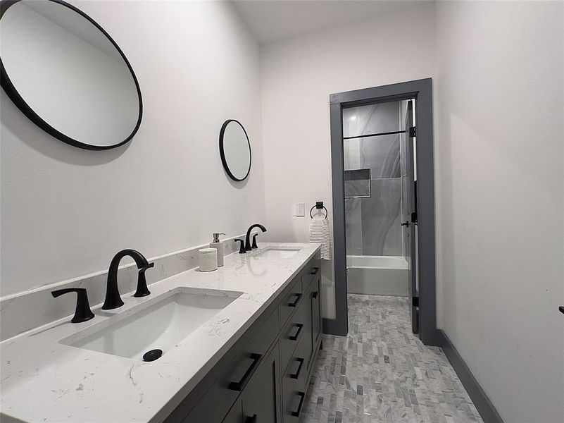 Bathroom featuring dual vanity, tiled shower /bath combo, and tile/patterned floors