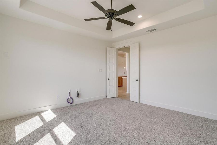 Carpeted empty room with sink, ceiling fan, and a raised ceiling