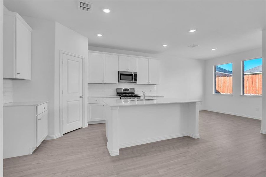 Kitchen featuring an island with sink, stainless steel appliances, white cabinets, and light hardwood / wood-style flooring