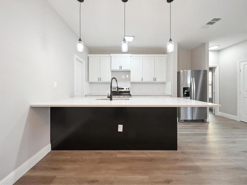 Kitchen featuring pendant lighting, stainless steel fridge, white cabinetry, and sink