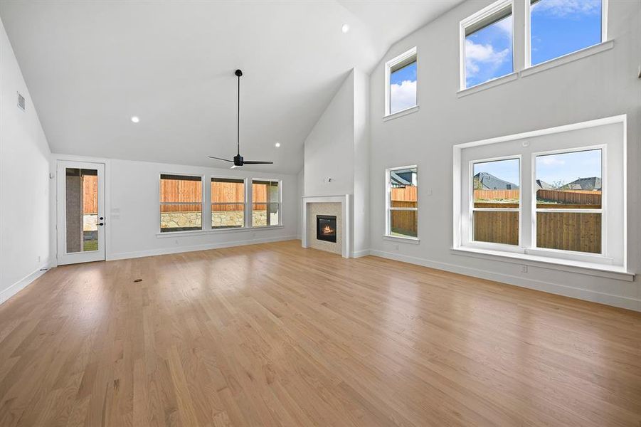 Unfurnished living room with high vaulted ceiling, healthy amount of natural light, a glass covered fireplace, a ceiling fan, and recessed lighting Unfurnished living room with high vaulted ceiling, healthy amount of natural light, a glass covered fireplace, a ceiling fan, and recessed lighting