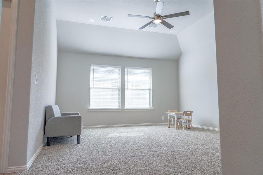 Living area featuring carpet, a ceiling fan, a textured wall, and vaulted ceiling