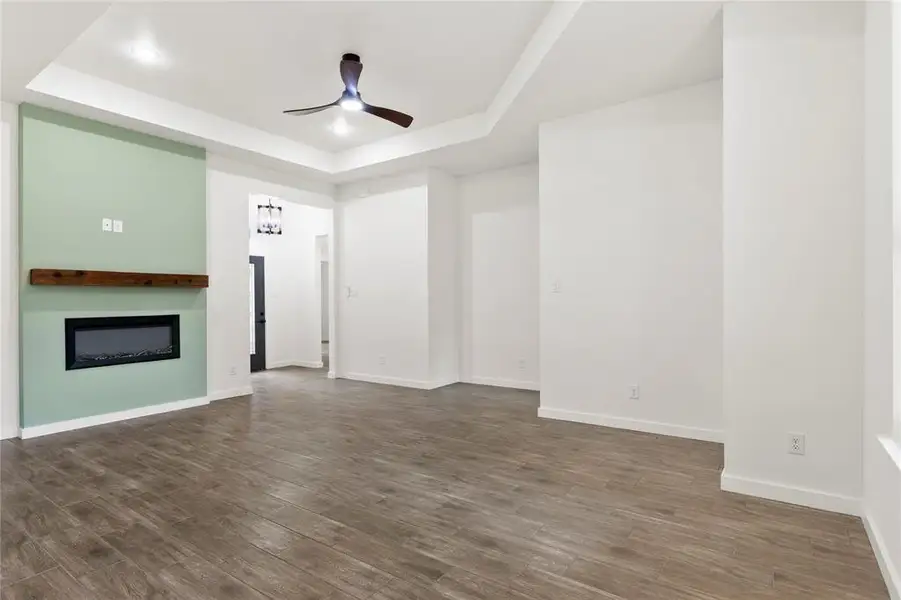 Spacious living area featuring wood-finish flooring, a contemporary electric fireplace with a wood mantle, and a tray ceiling with recessed lighting