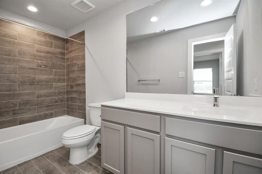 The secondary bath includes modern tile flooring, a combined bath and shower with a tile surround, light wood cabinetry, and a beautiful light-colored countertop. Sample photo of completed home with similar floor plan. Actual colors and selections may vary.