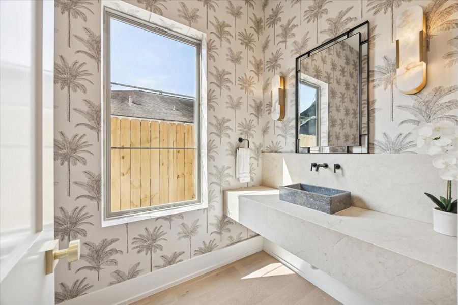 This charming first floor powder bath is sure to impress, featuring stylish wallpaper, a stunning light fixture, and elegant marble finishes.