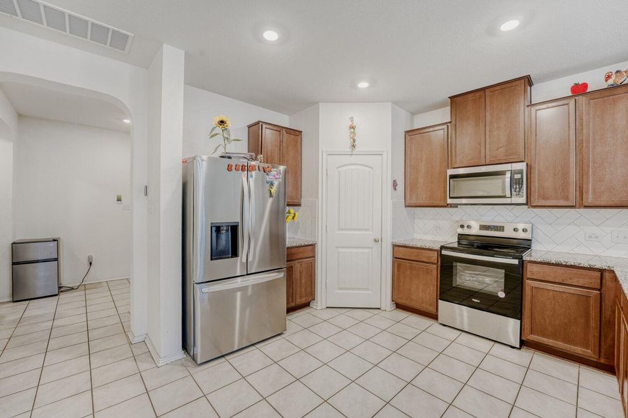 Kitchen featuring appliances with stainless steel finishes, light stone countertops, backsplash, light tile patterned floors, and brown cabinets