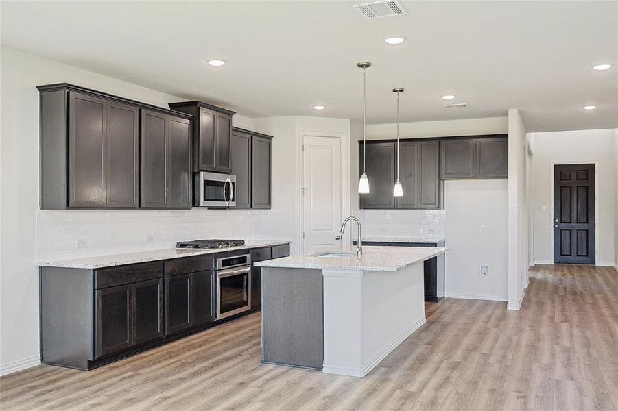 Kitchen with a center island with sink, tasteful backsplash, light hardwood / wood-style floors, stainless steel appliances, and light stone counters