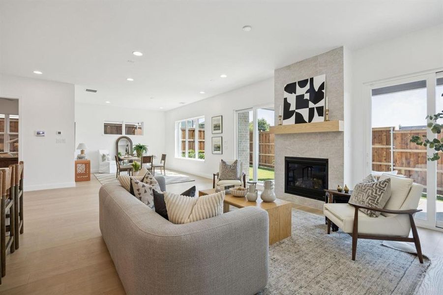 Open-concept living area with light wood-finish flooring, recessed lighting, and a modern fireplace featuring a light-toned tile surround and wood mantel