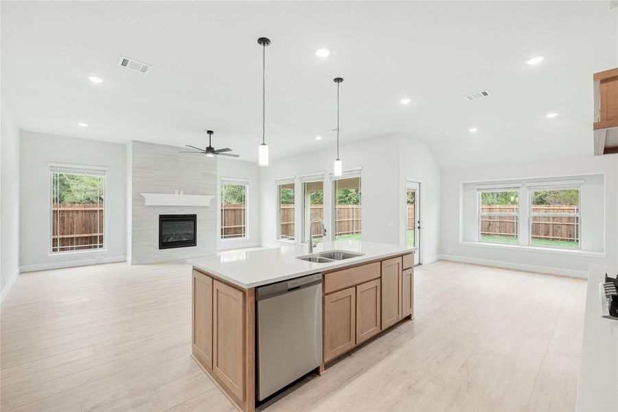 Open-concept kitchen with center island, sink, dishwasher, and living area with fireplace in background
