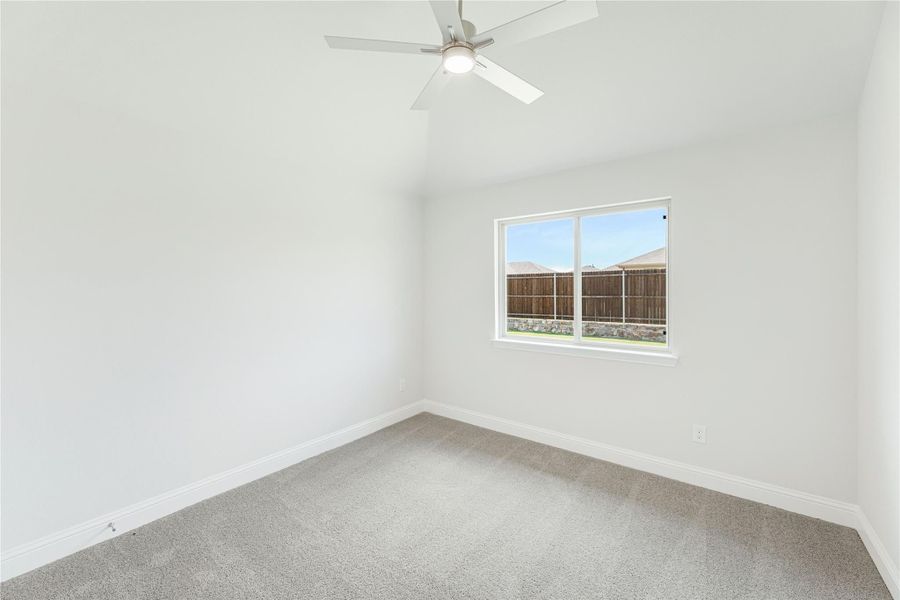Empty bedroom with vaulted ceiling, ceiling fan, carpet flooring, and single window overlooking backyard fence. Empty bedroom with vaulted ceiling, ceiling fan, carpet flooring, and single window overlooking backyard fence.