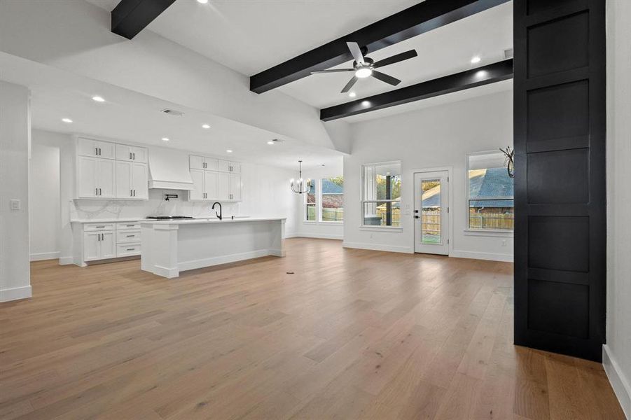 Unfurnished living room with recessed lighting, a chandelier, light wood-style flooring, beam ceiling, and ceiling fan