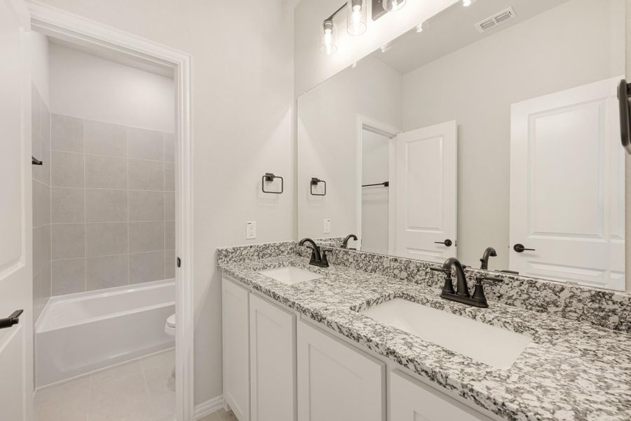 Bathroom with double sink vanity, granite countertops, white cabinets, and tiled tub-shower combo