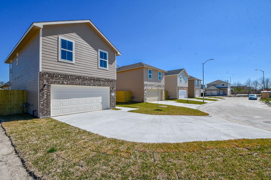New suburban homes with two-story designs, attached garages, and manicured lawns on a sunny day with clear blue skies.