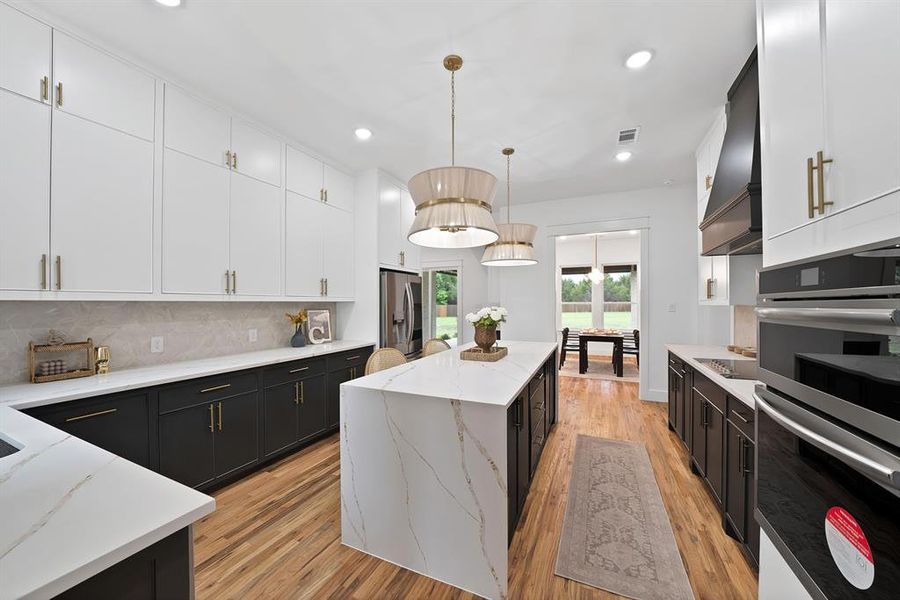 The kitchen features hardwood flooring, white and dark cabinetry with gold-toned hardware, white countertops, and a kitchen island with a white countertop