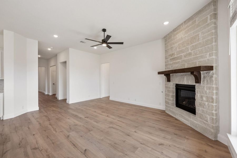 Open living room with stone fireplace, wood mantel, hardwood floors, and ceiling fan Open living room with stone fireplace, wood mantel, hardwood floors, and ceiling fan