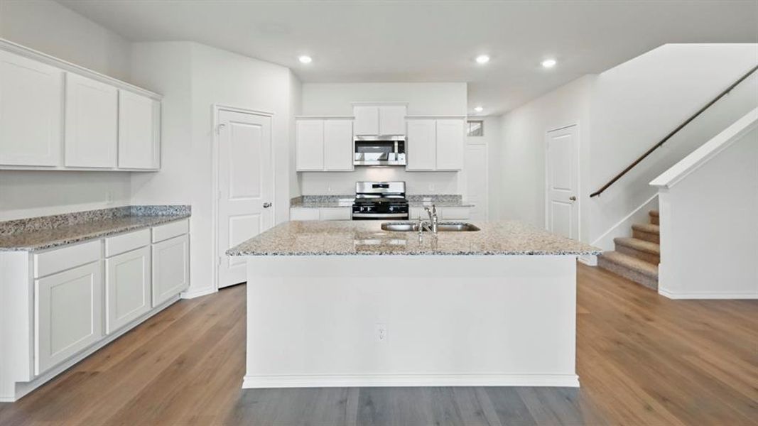 Kitchen featuring white cabinets, light stone countertops, stainless steel appliances, a center island with sink, and light wood-style floors