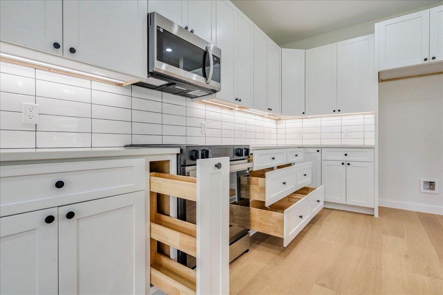 A well-lit kitchen with sleek white cabinetry and many integrated storage solutions.