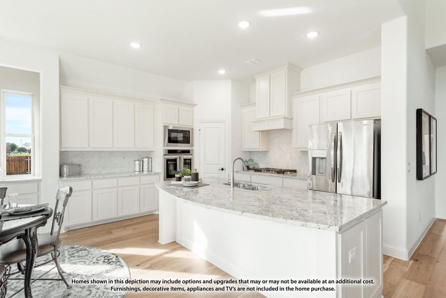 White kitchen with curved granite island, stainless steel appliances, double ovens, and light hardwood floors