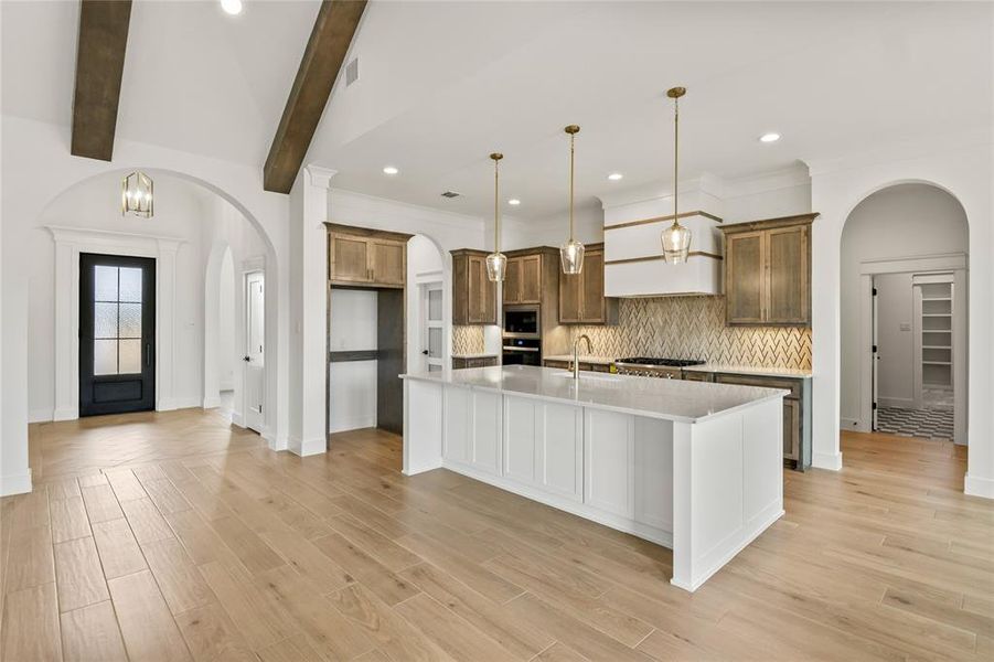 Gourmet kitchen featuring a large central island with a quartz countertop, custom cabinetry, a mosaic tile backsplash, and recessed lighting