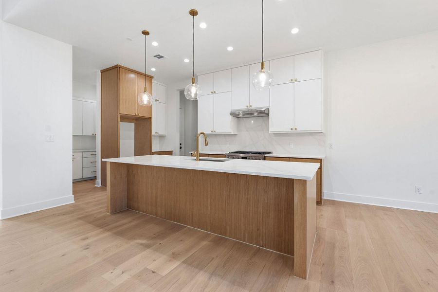 A spacious kitchen highlights a broad central island set against light hardwood flooring.
