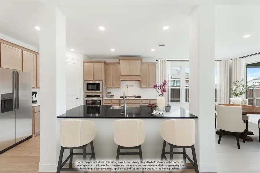 Kitchen with light wood cabinets, dark island with three bar stools, and stainless steel appliances