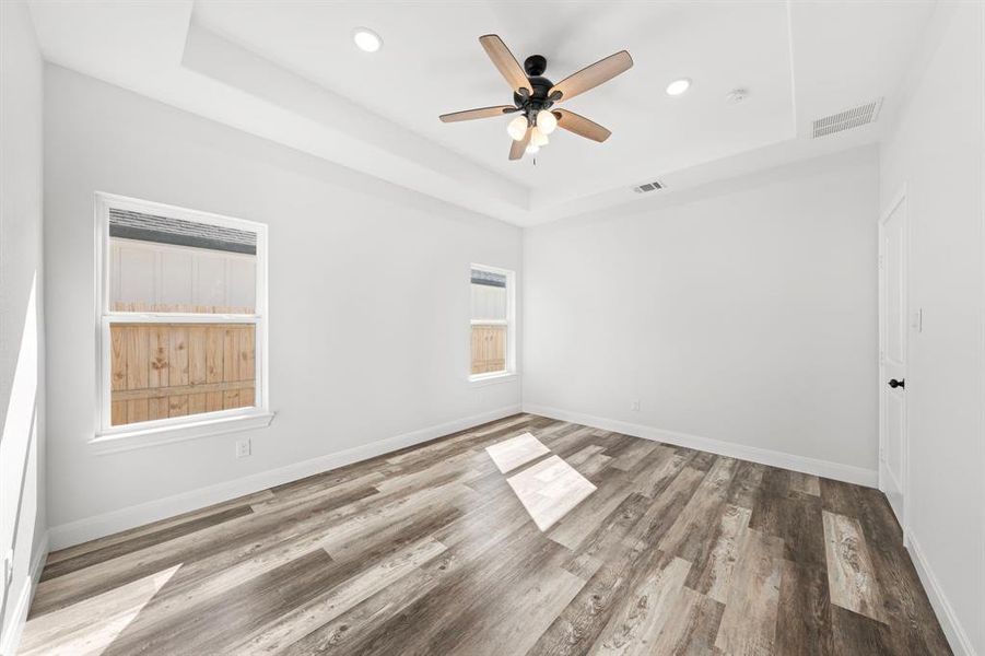 Empty room featuring a tray ceiling, wood finished floors, ceiling fan, and recessed lighting Empty room featuring a tray ceiling, wood finished floors, ceiling fan, and recessed lighting