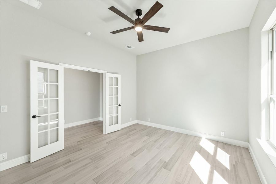 Empty room with light wood floors, ceiling fan, and white French doors Empty room with light wood floors, ceiling fan, and white French doors