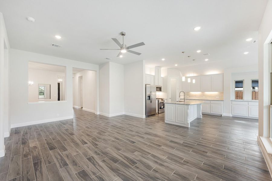 Open living area with wood-look tile floors, ceiling fan, and white kitchen with island and stainless appliances