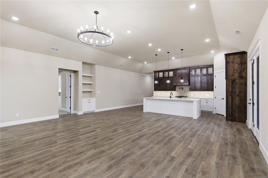 Open-concept living area featuring wood-finish flooring, recessed lighting, and a contemporary chandelier Open-concept living area featuring wood-finish flooring, recessed lighting, and a contemporary chandelier
